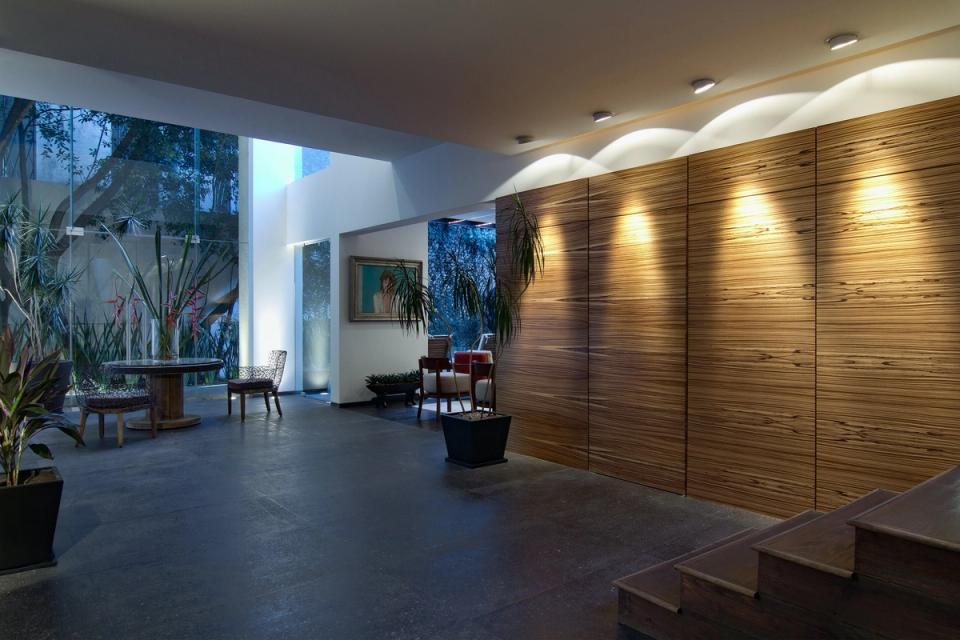 Vestíbulo al anochecer con muro de madera y jardín interior tras el cristal