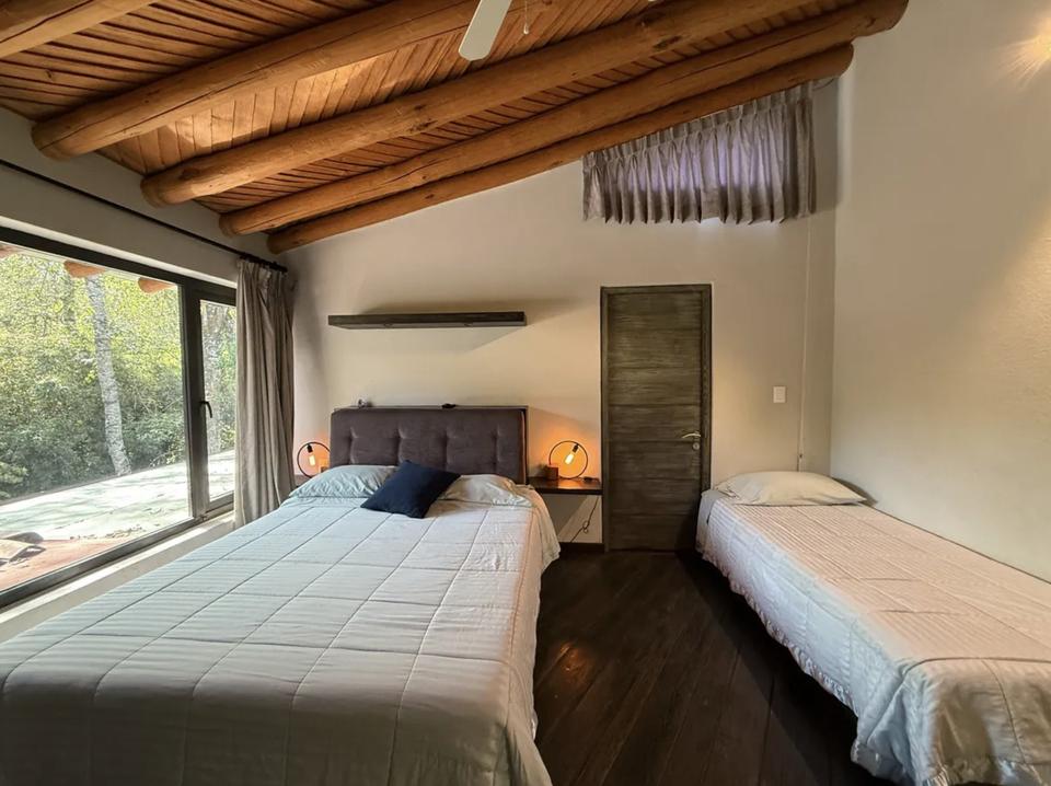 Recámara con dos camas bajo vigas de madera junto a un ventanal