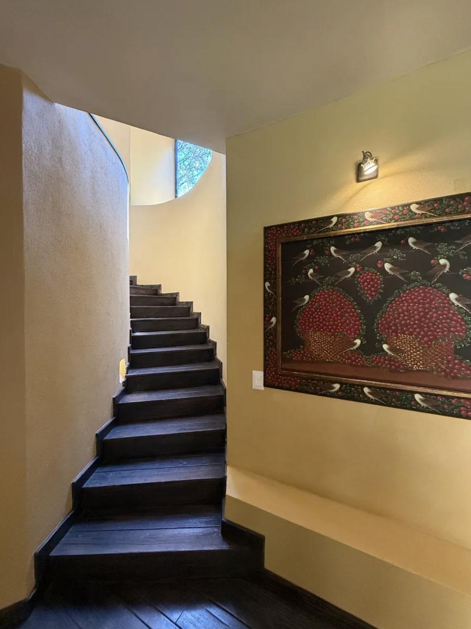 Escalera de madera oscura junto a un muro curvo con ventana alta
