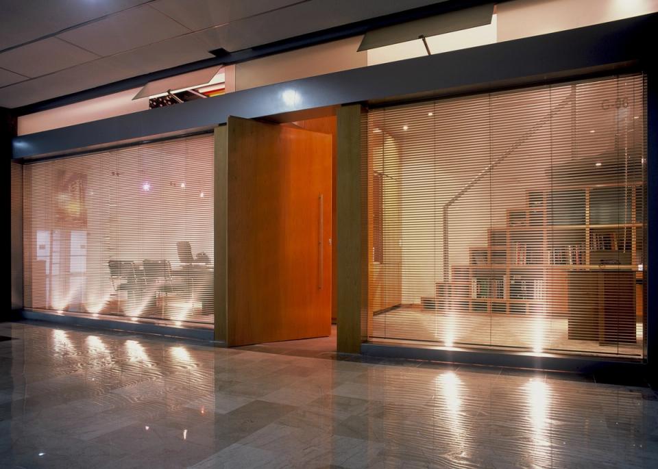 Fachada de cristal de la oficina con persianas y puerta de madera abierta
