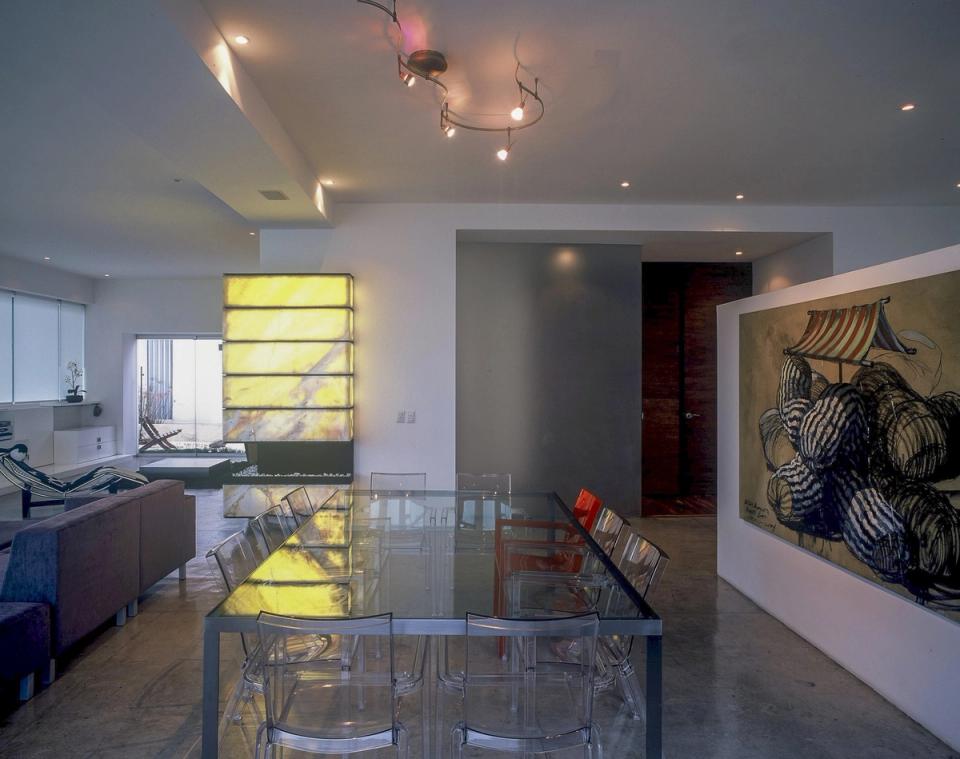 Comedor con mesa de cristal y sillas transparentes frente a la chimenea iluminada