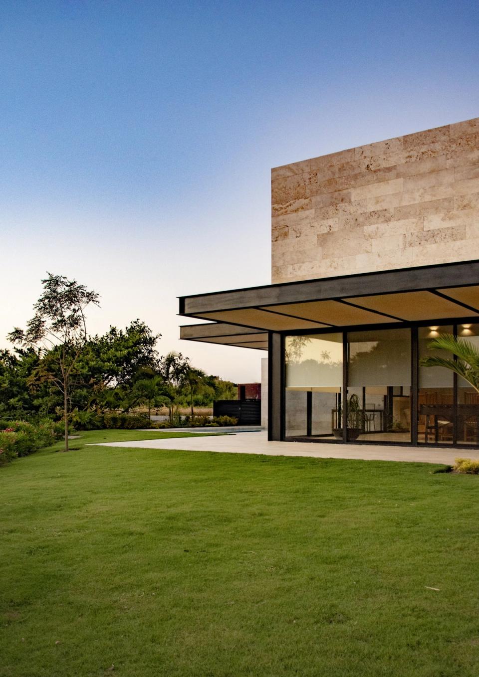 La casa desde el jardín, con alero de acero y volumen de piedra