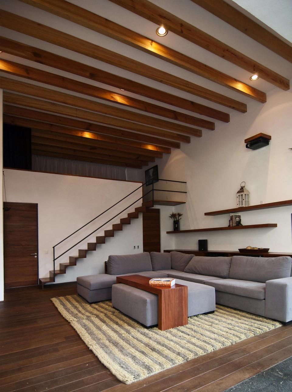 Sala de doble altura con vigas y escalera de madera hacia el tapanco