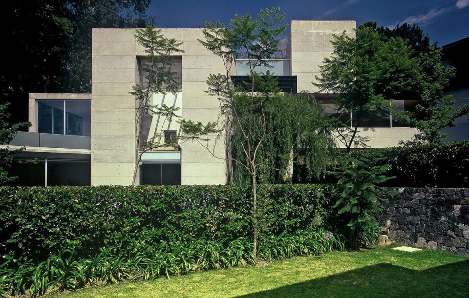 Fachada de concreto hacia el jardín con setos y muro de piedra