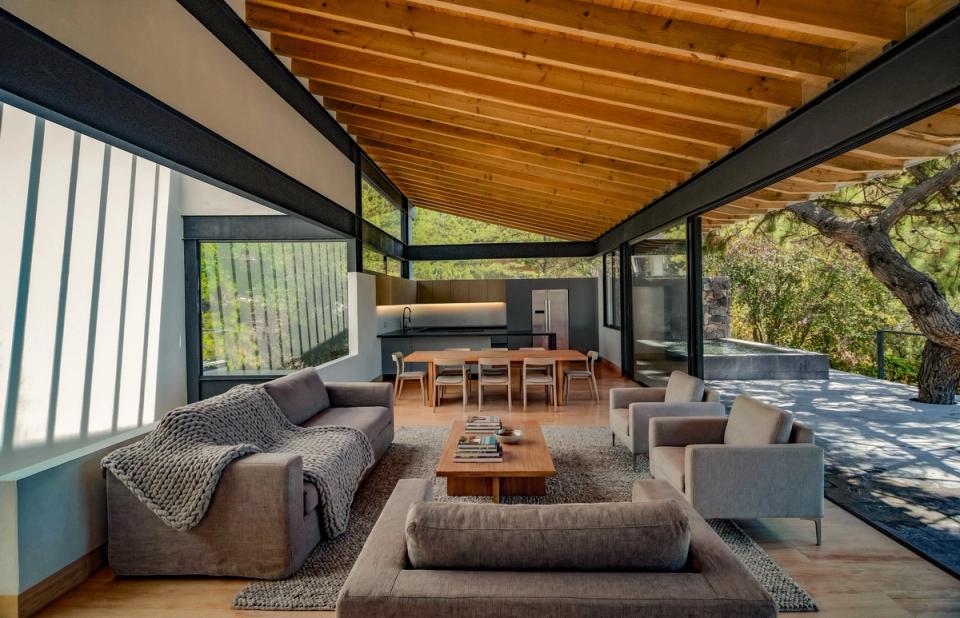 Sala bajo techo inclinado de madera con ventanales hacia el bosque