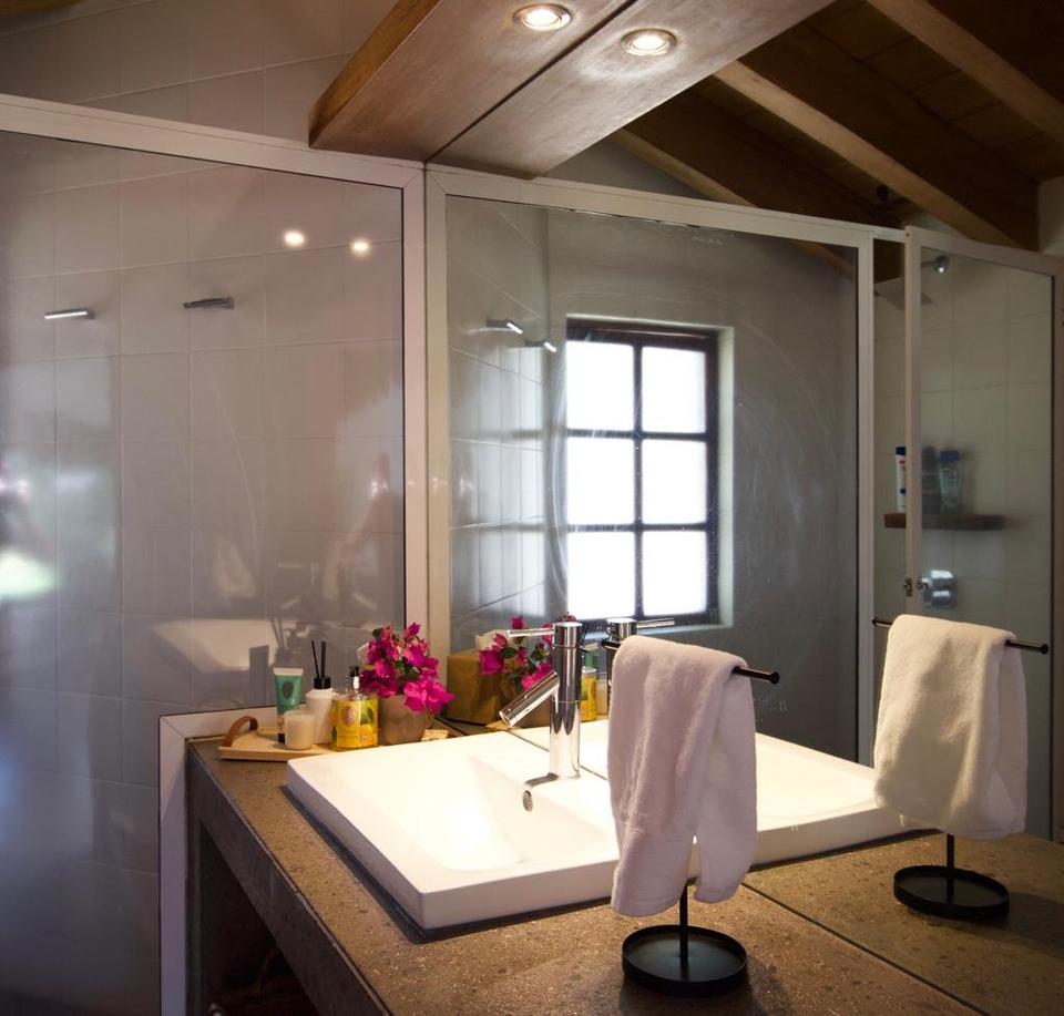 Baño con lavabo blanco, cancel de vidrio y vigas de madera