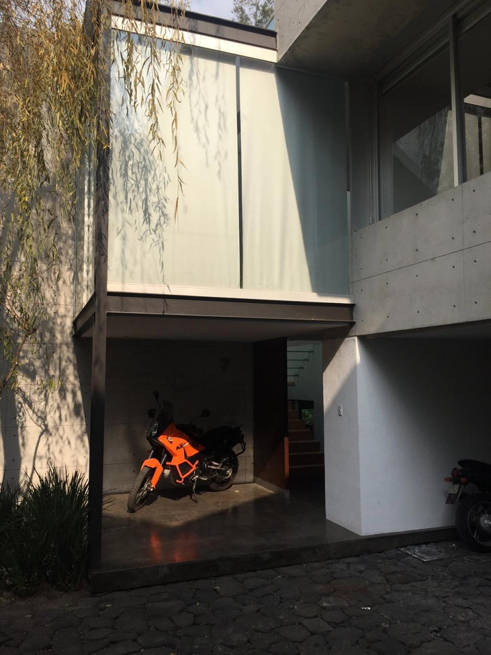 Cochera con motocicleta bajo un volumen de cristal y escalera al fondo