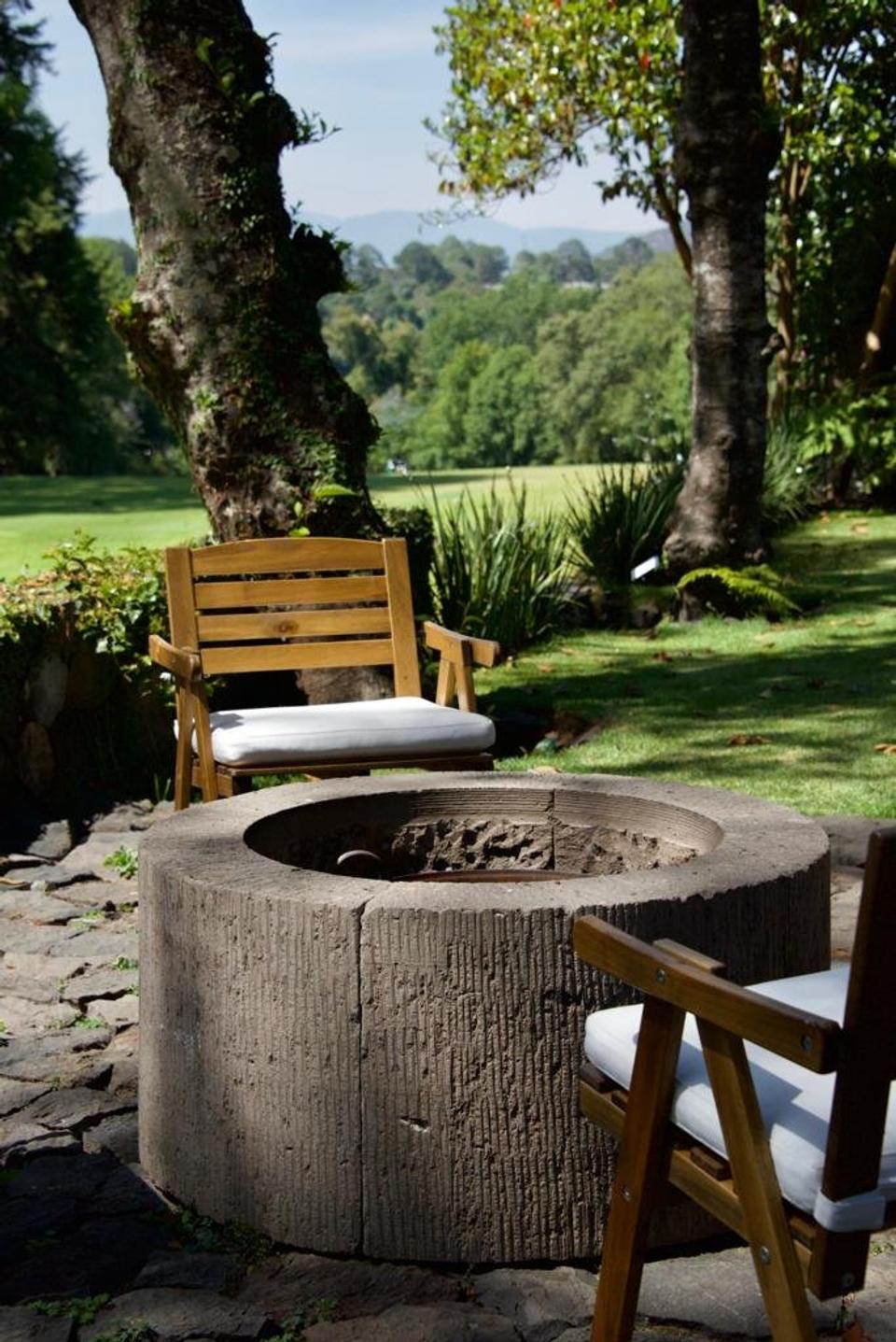 Fogatero circular con sillas de madera entre los árboles del jardín