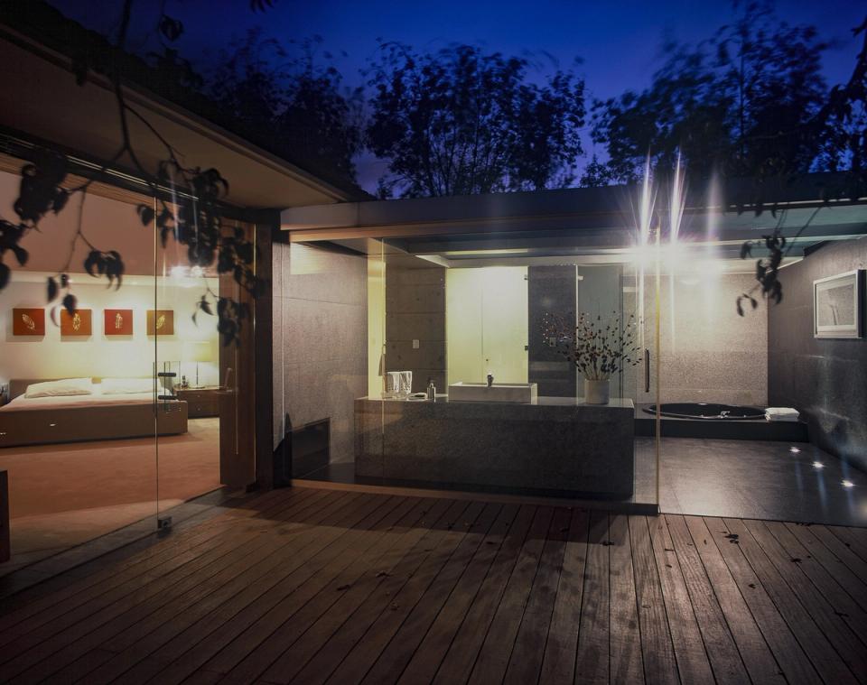 Recámara y baño de cristal vistos de noche desde la terraza de madera