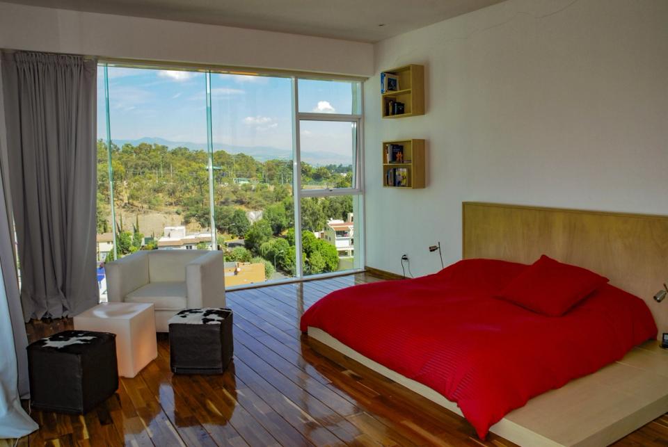 Recámara con ventanal de piso a techo y vista a los árboles