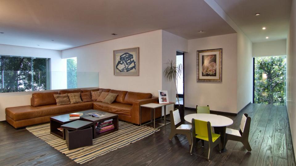 Sala con sofá de piel, piso de madera y barandal de cristal