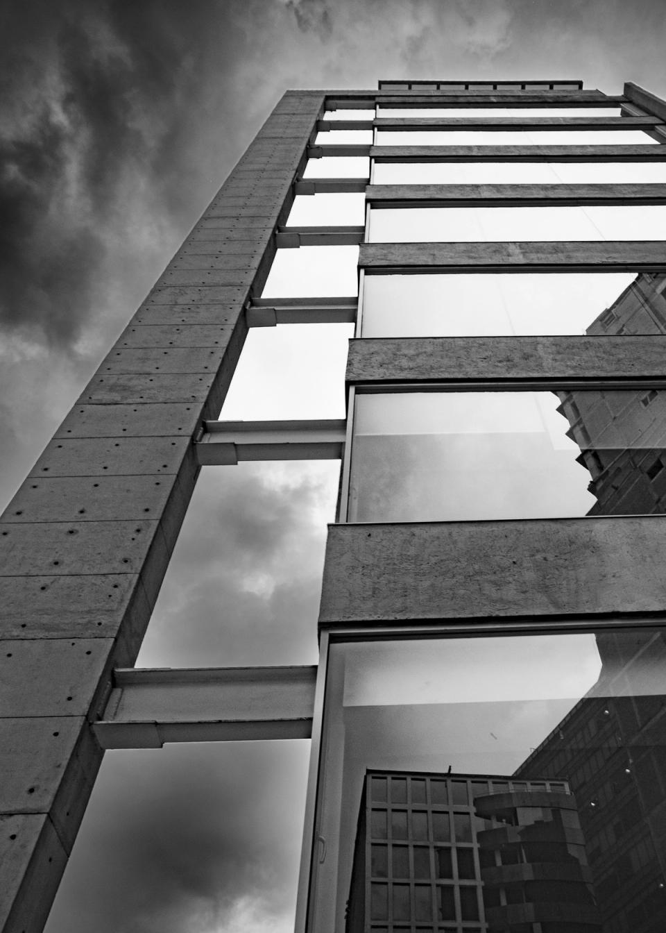 Muro de concreto aparente y ventanales contra un cielo nublado, en blanco y negro