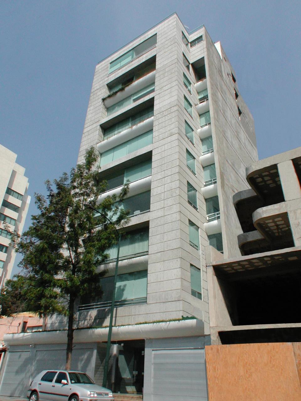 Torre de departamentos con balcones de cristal entre árboles