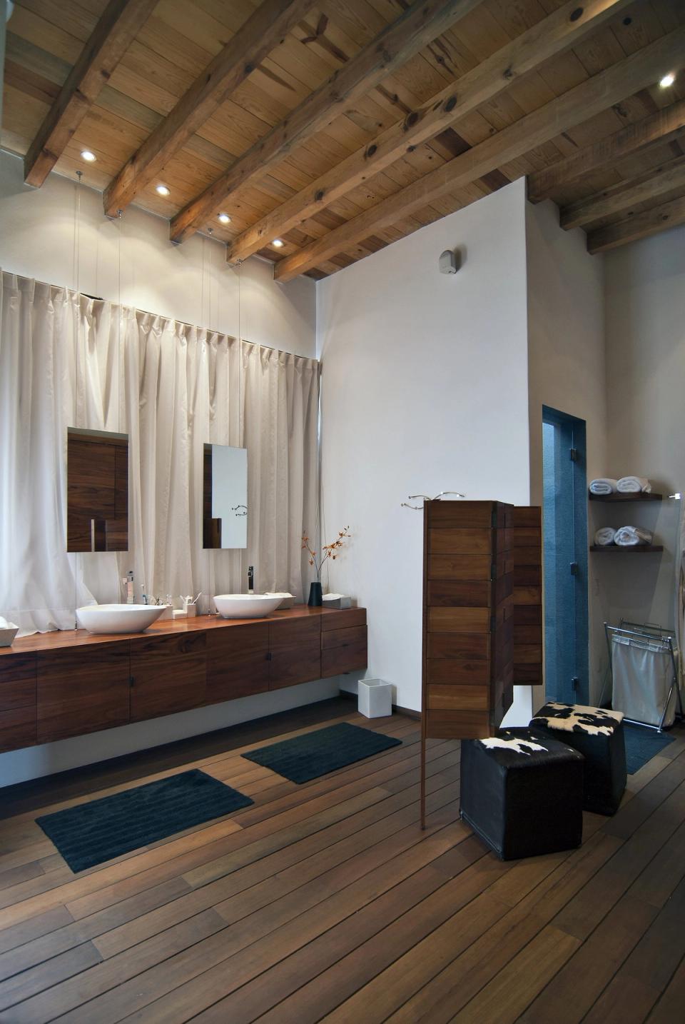 Baño con doble lavabo sobre mueble de madera y techo de vigas