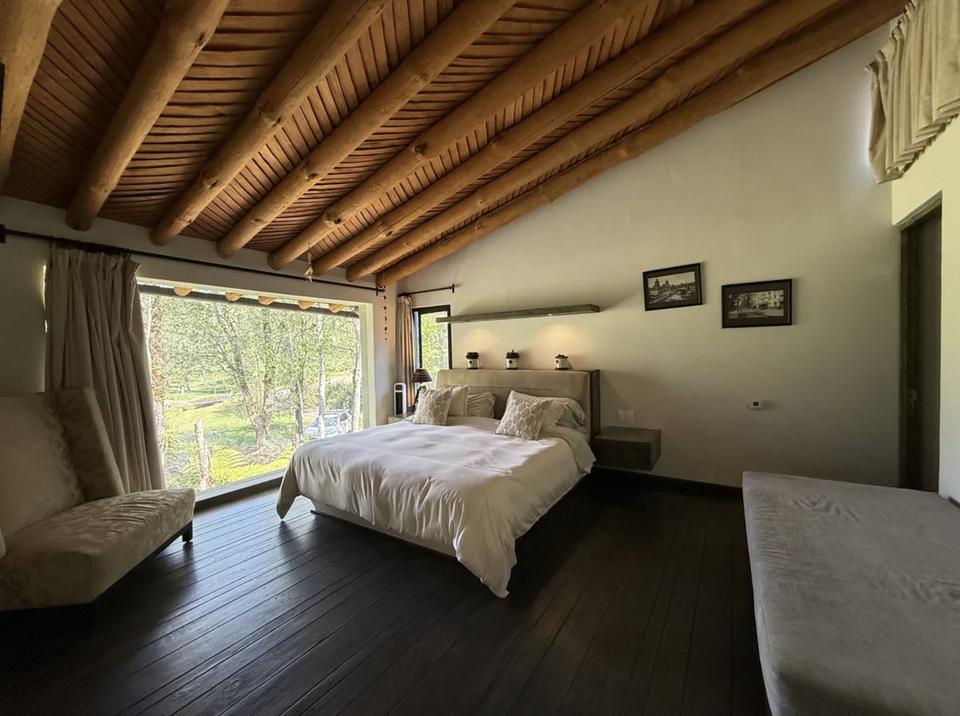 Recámara con ventanal hacia los árboles bajo un techo inclinado de madera