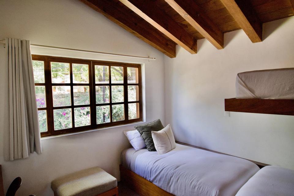 Recámara bajo techo inclinado de vigas de madera con ventana hacia los árboles