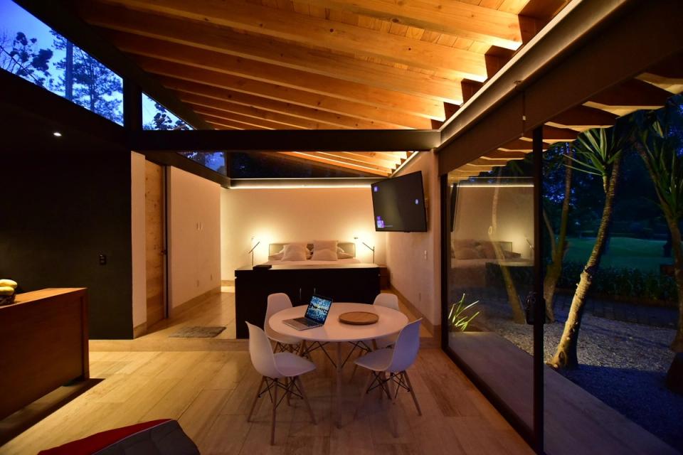 Comedor y recámara bajo techo de madera con muro de vidrio al anochecer