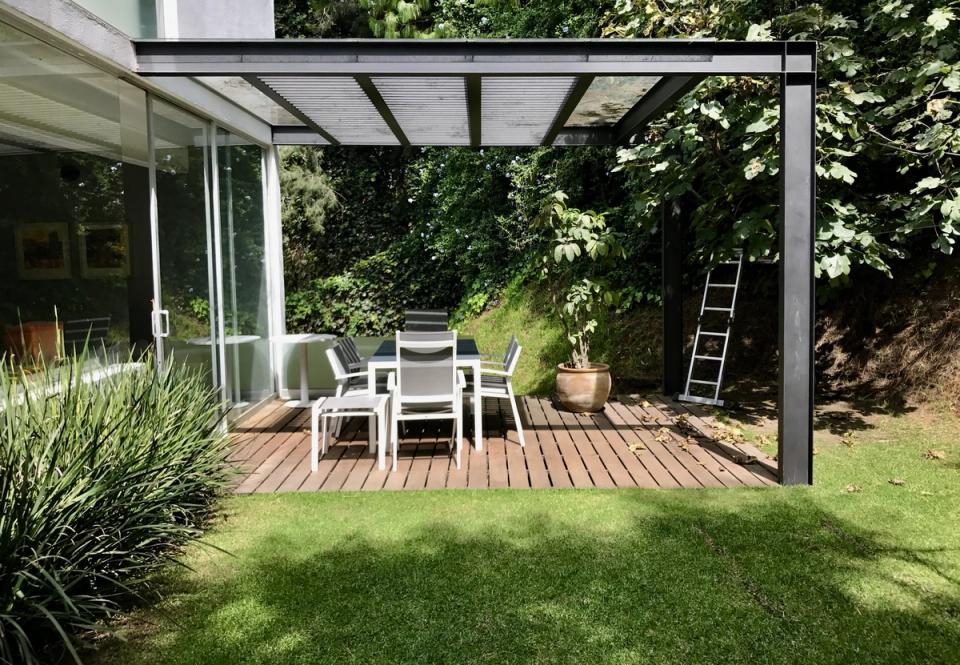 Terraza de madera bajo pérgola metálica junto al jardín