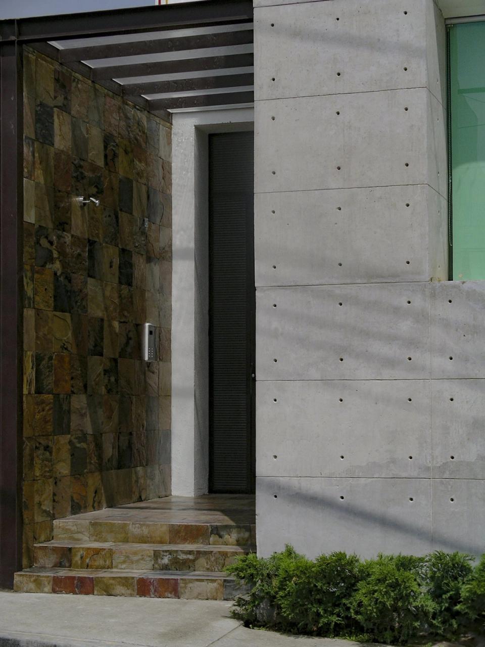 Puerta de acceso entre un muro de piedra y el concreto aparente