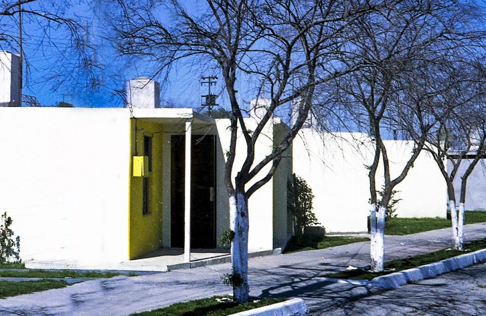 Casa de muros blancos con puerta amarilla y árboles en la banqueta