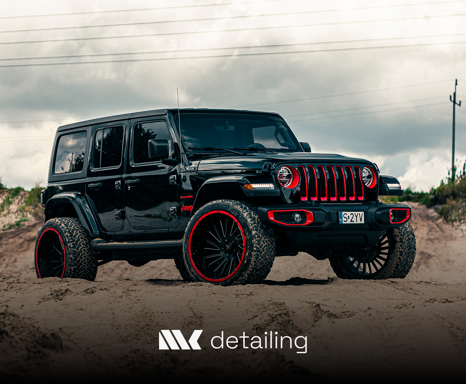 A customized black Jeep Wrangler with red accents features oversized wheels, aggressive off-road tires, and distinctive red trim on its signature grille.