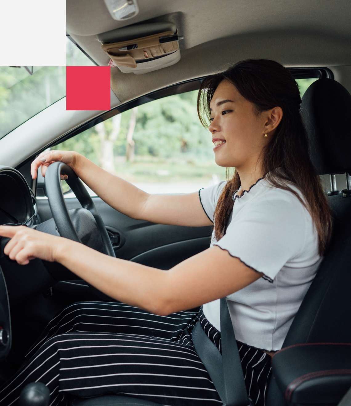 A driver in a white top and striped skirt sits behind the wheel of a car with a content expression while driving on a sunny day.