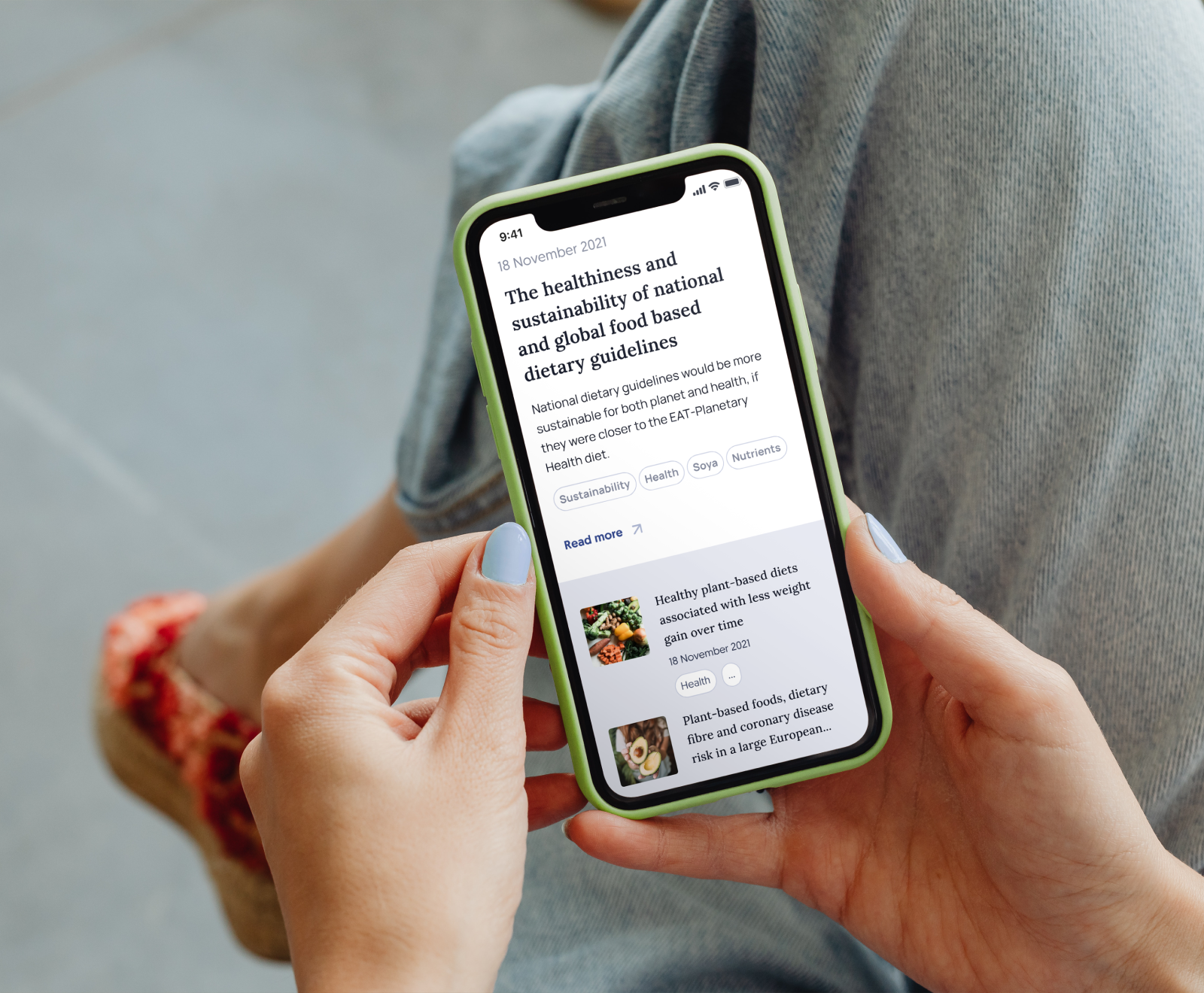 A smartphone displays an article about healthiness and sustainability of national and global food-based dietary guidelines, held by hands with light blue nail polish.