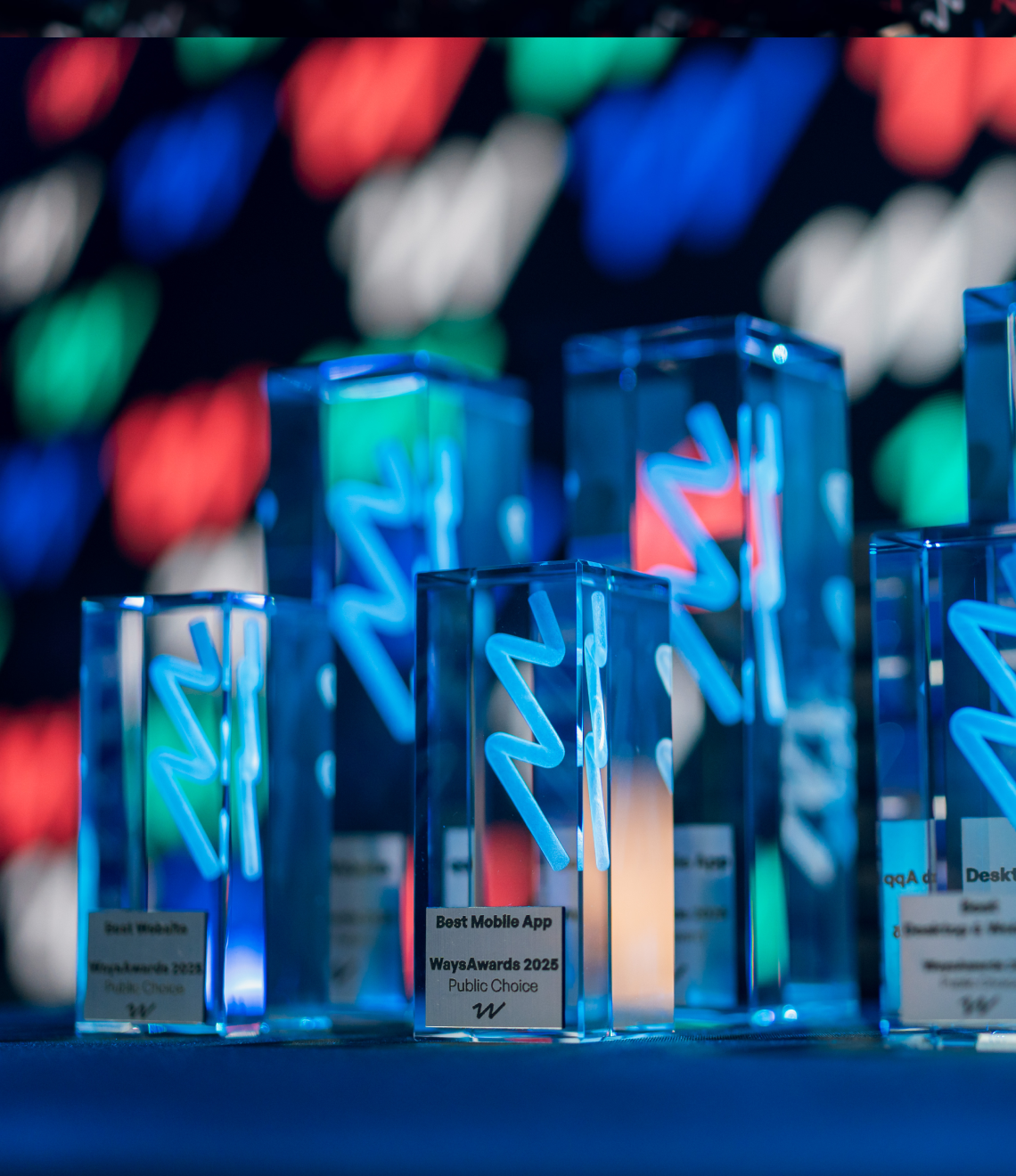 A row of translucent blue crystal trophies featuring neon-style zigzag designs stands on display at the 2023 Ways Awards ceremony.
