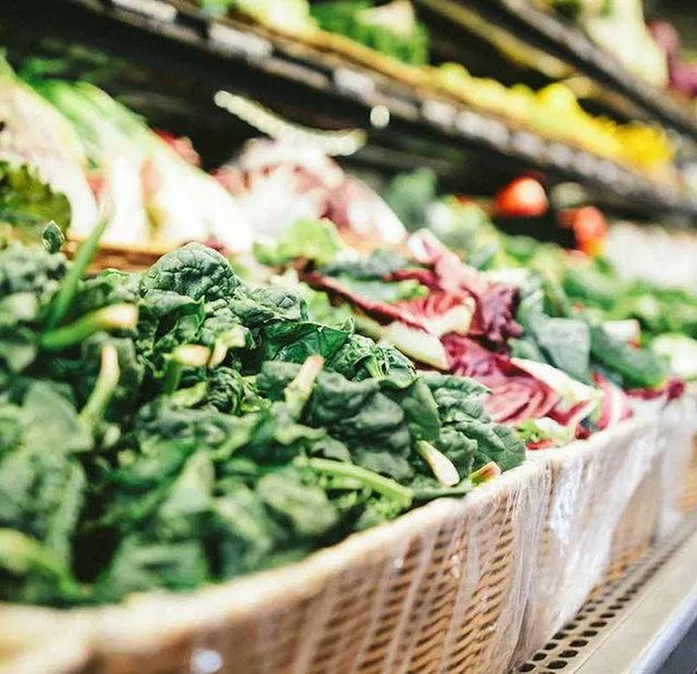 Fresh leafy greens and red lettuce varieties are neatly displayed in woven baskets at a produce market.
