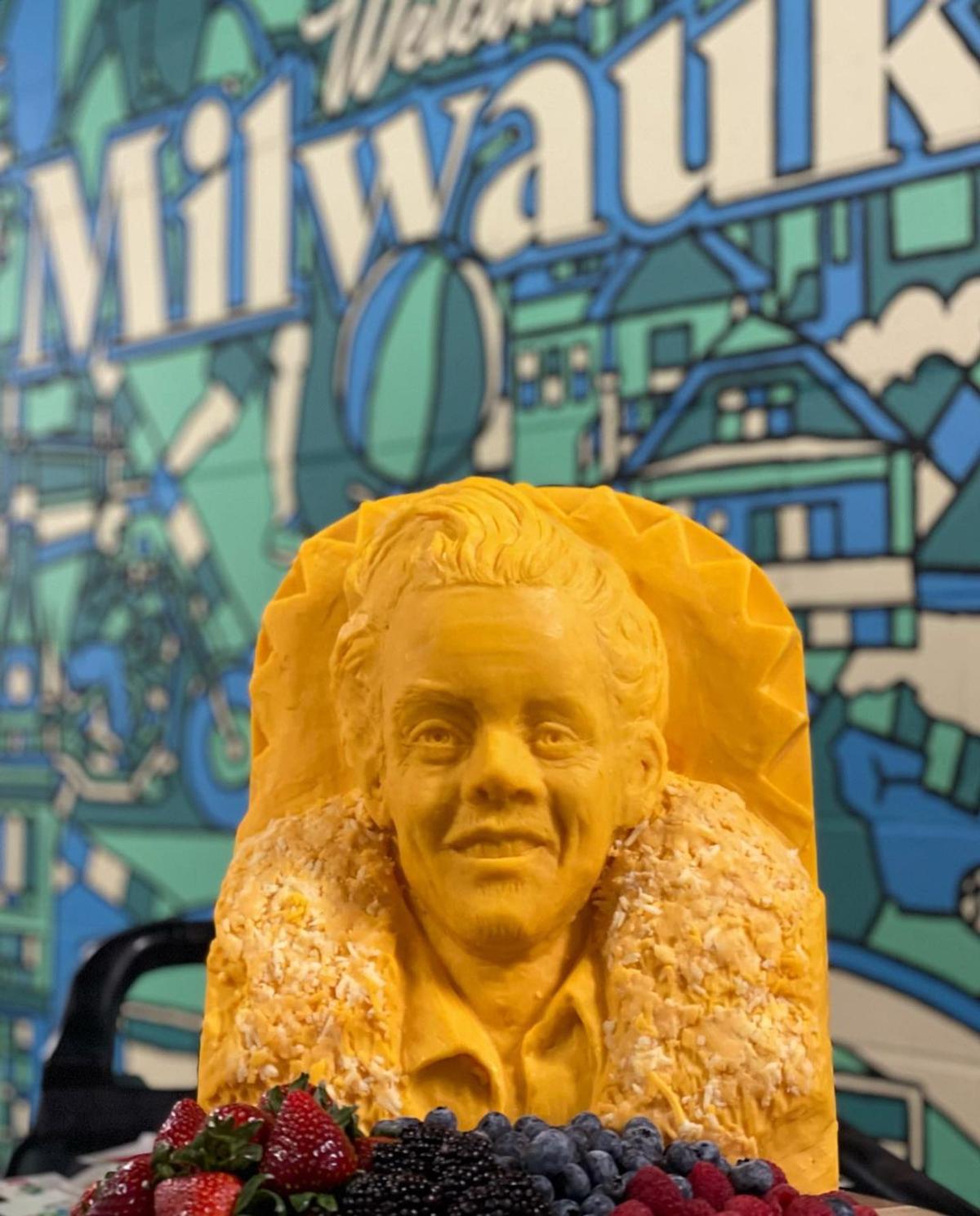 A cheese sculpture of Harry Styles in front of the Welcome to Milwaukee mural