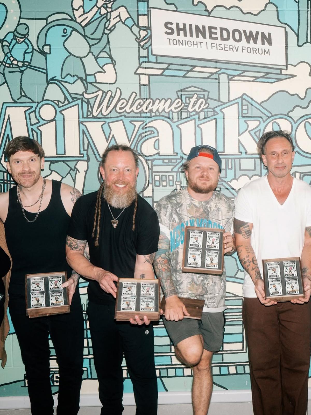 Shinedown holding framed gifts in front of the Welcome to Milwaukee mural