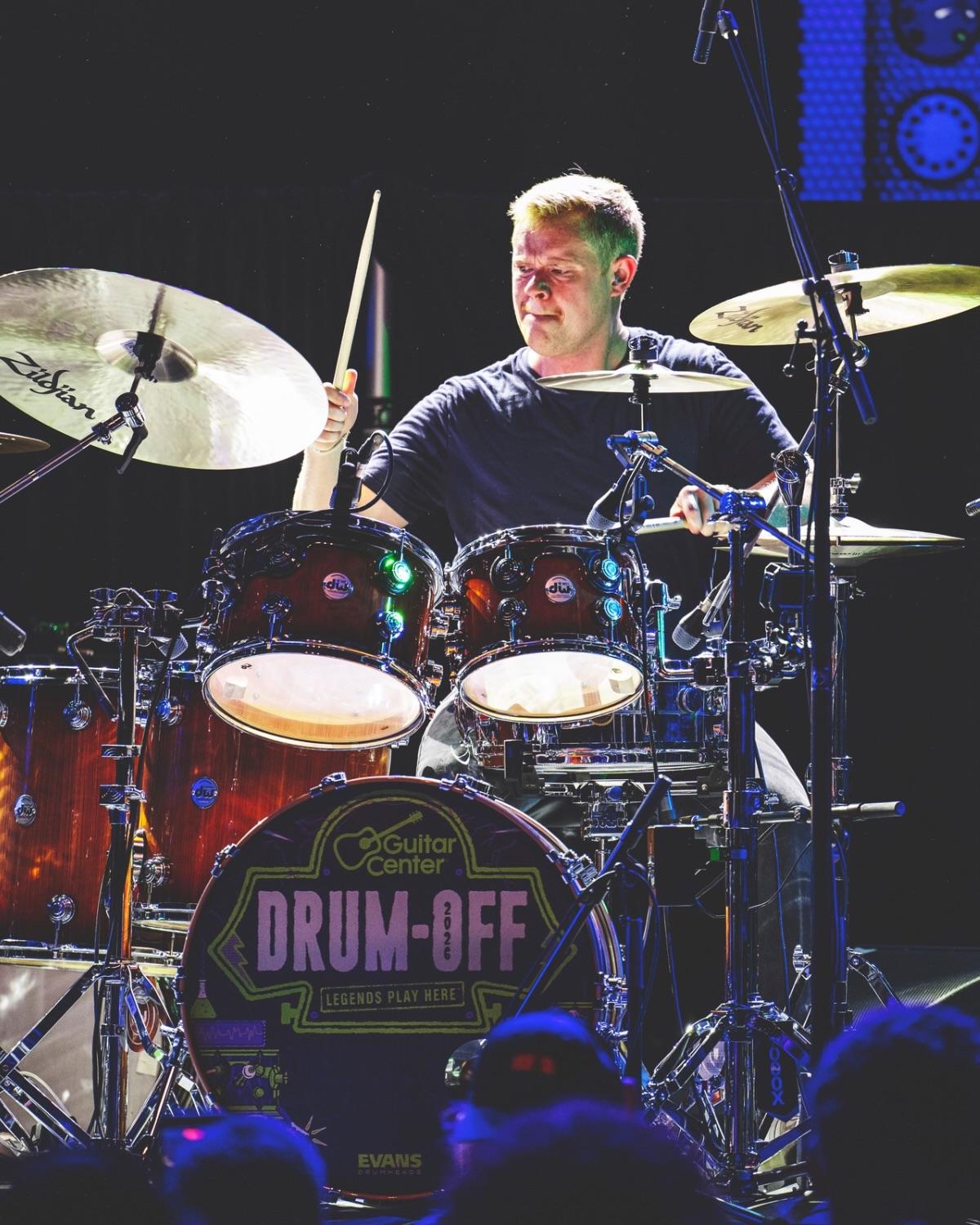 A drummer on stage behind a kick drum head printed with the Drum-Off logo