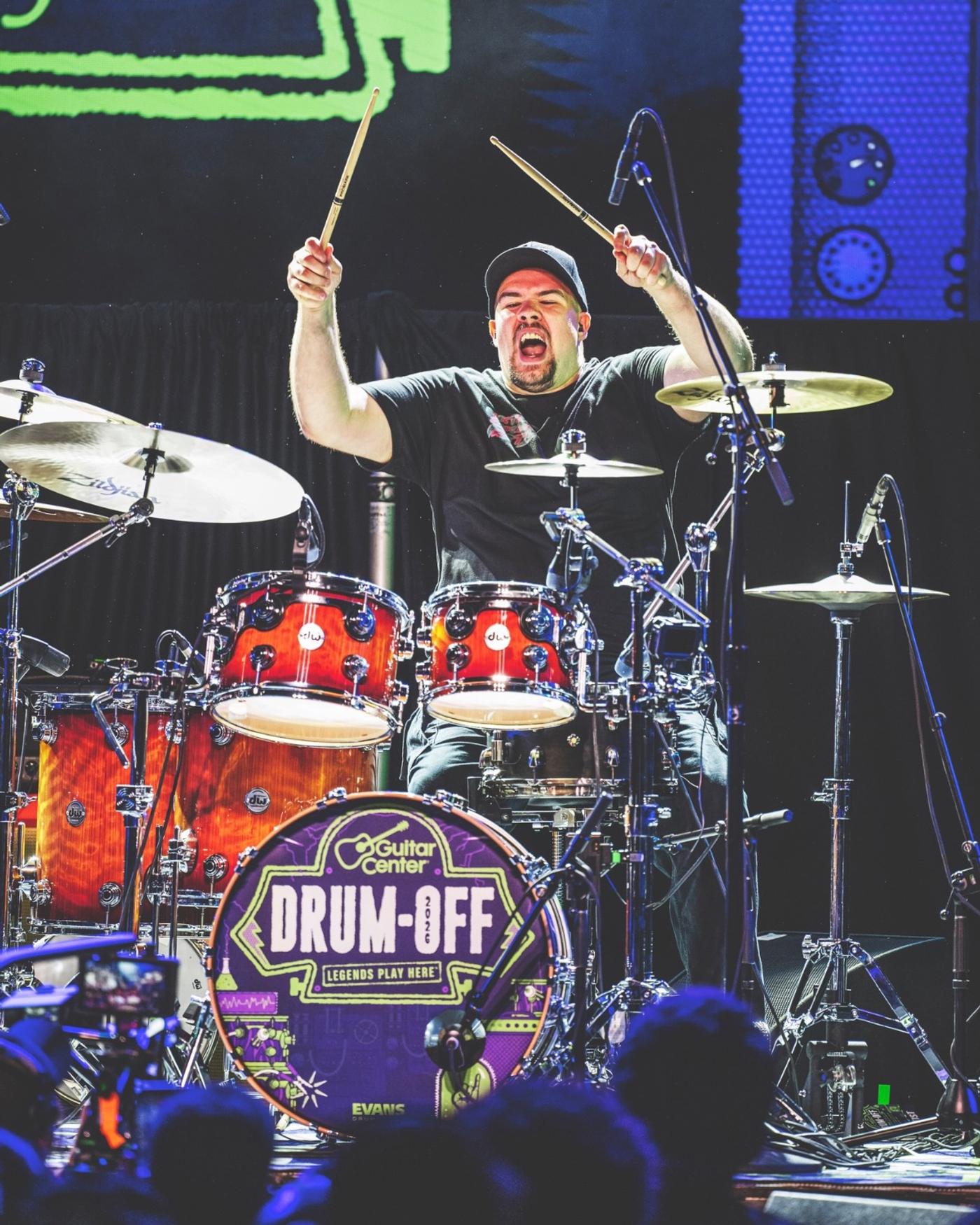 A drummer mid-hit behind a Drum-Off kick drum head