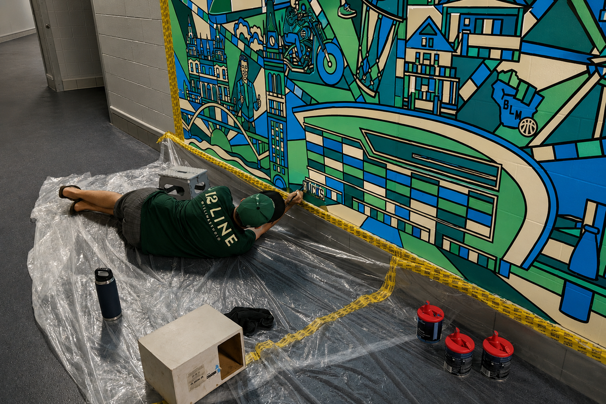 Nate painting the bottom edge of the Welcome to Milwaukee mural from a drop cloth