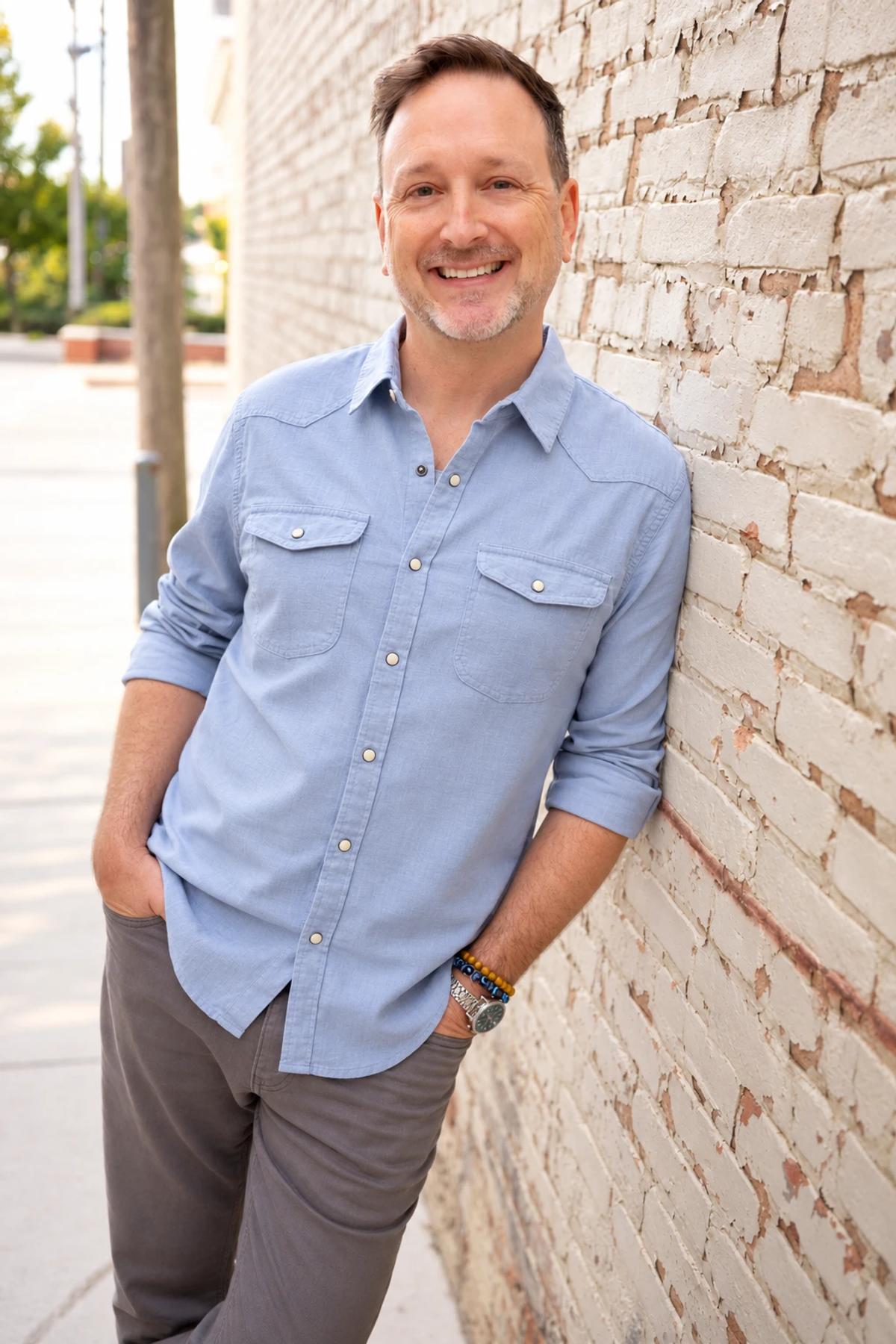 Nate Azark, founder of 12 Line Studio, leaning against a painted brick wall.