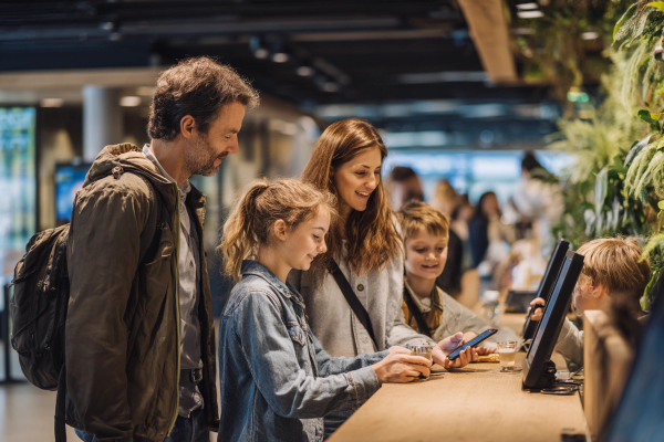 a family standing at a counter booking tickets with a smartphone