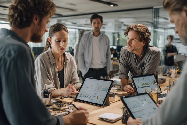 a group of people sitting around a table looking at a tablet with a graph on it