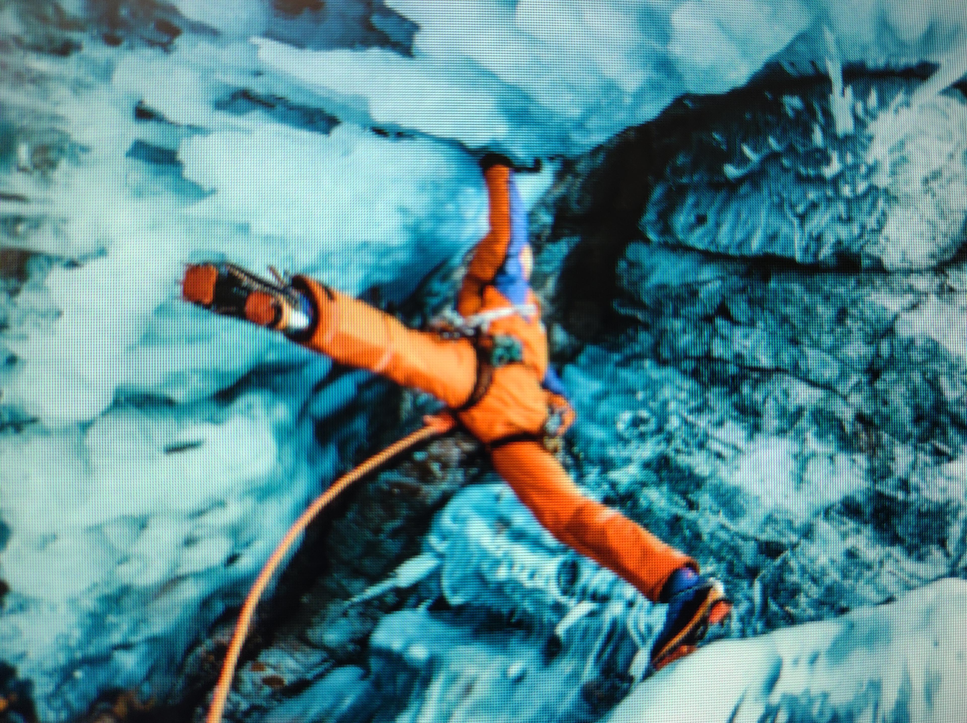 Mountaineer athlete Dani Arnold explores the deepest lake on earth.  His legs are fully extended in a "spread eagle" position as he makes a perilous climb up a very steep and treacherous ice-covered mountain.