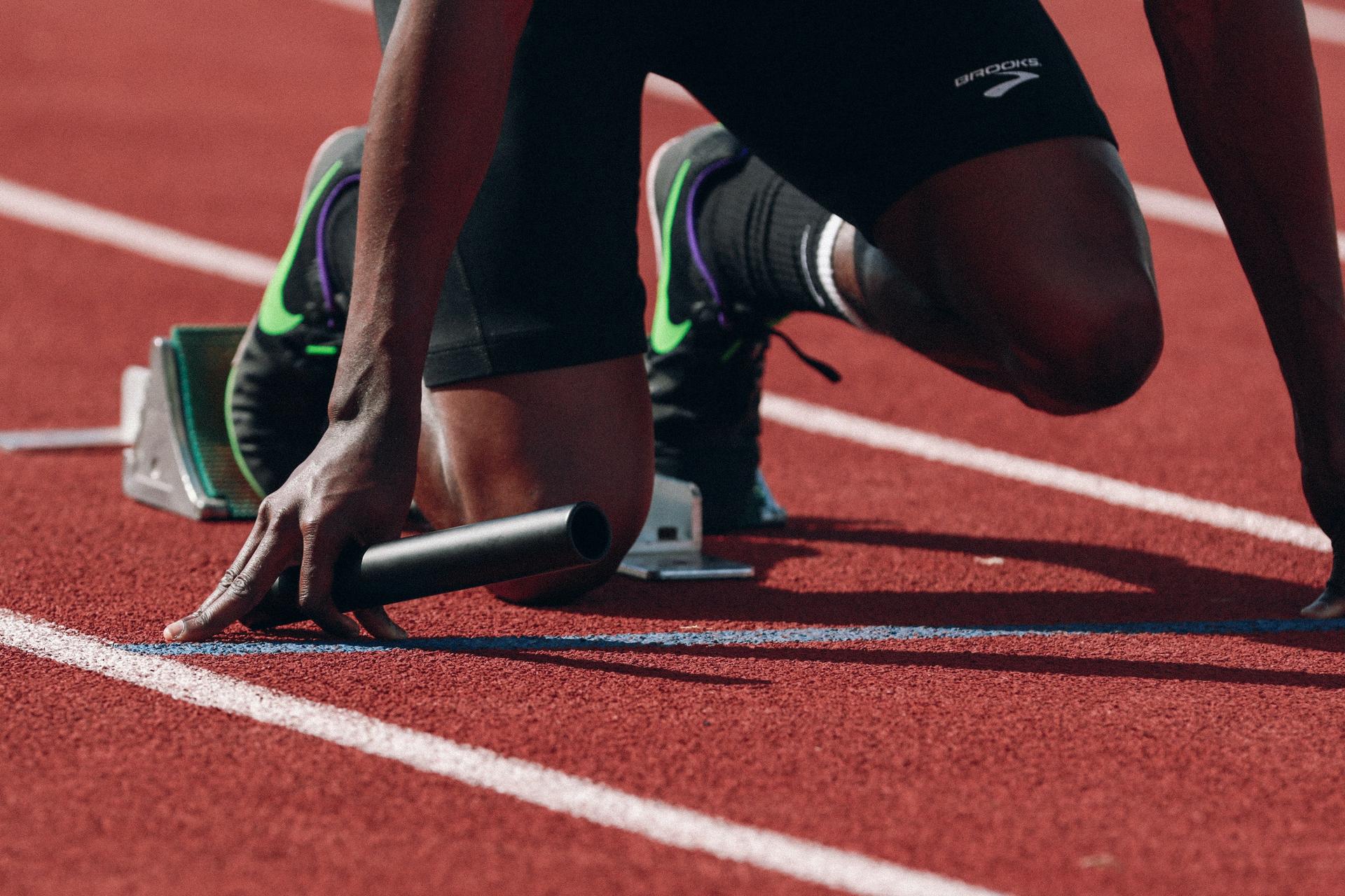 Closeup of track athlete's legs preparing to sprint holding baton.