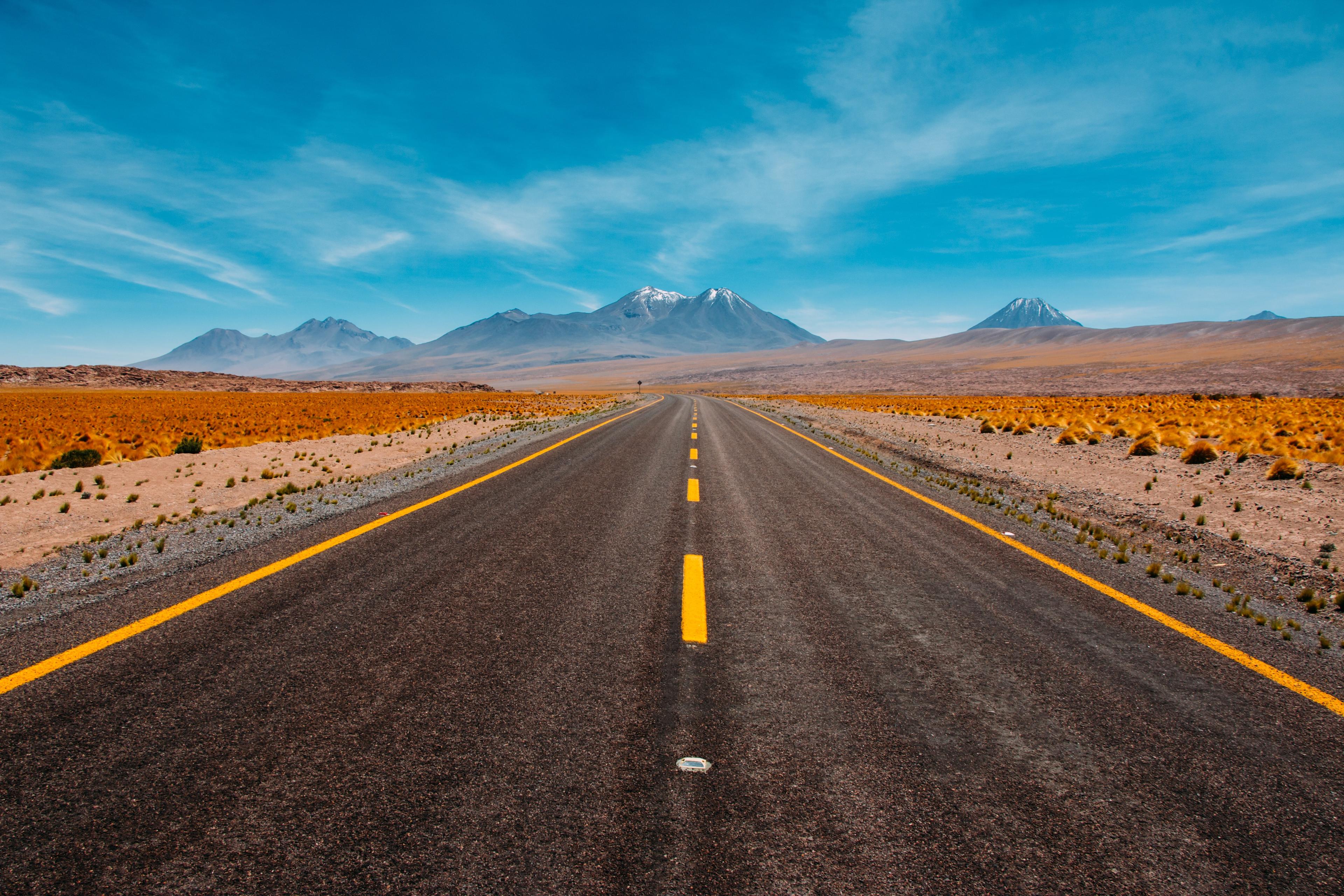 A rural paved one-lane road, with snow-peaked mountains in the far distance.  A glorious blue sky abounds.