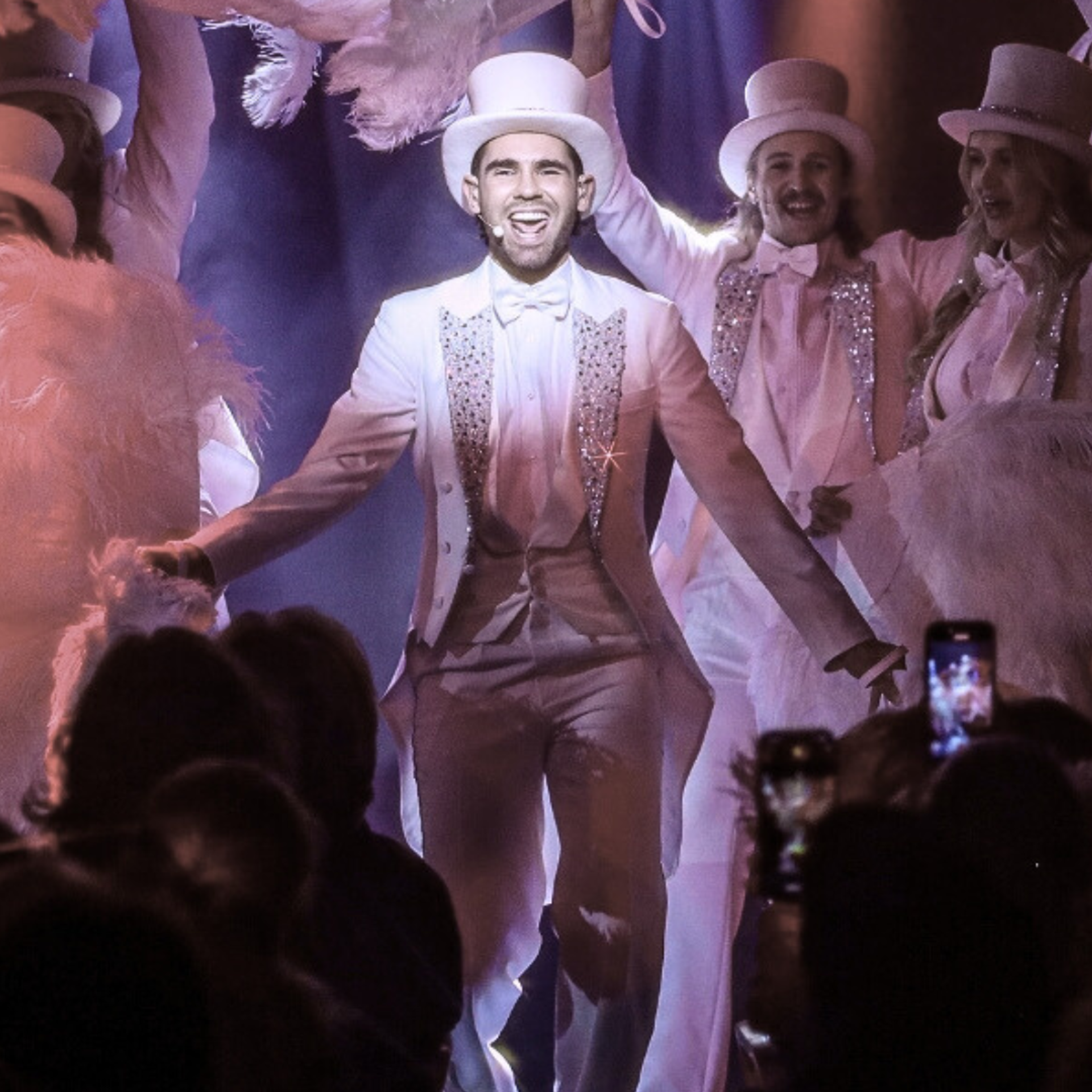 Golden Hits show. En man i vit frack som glittrar och hög hatt. Han sjunger och är omgiven av andra artister.