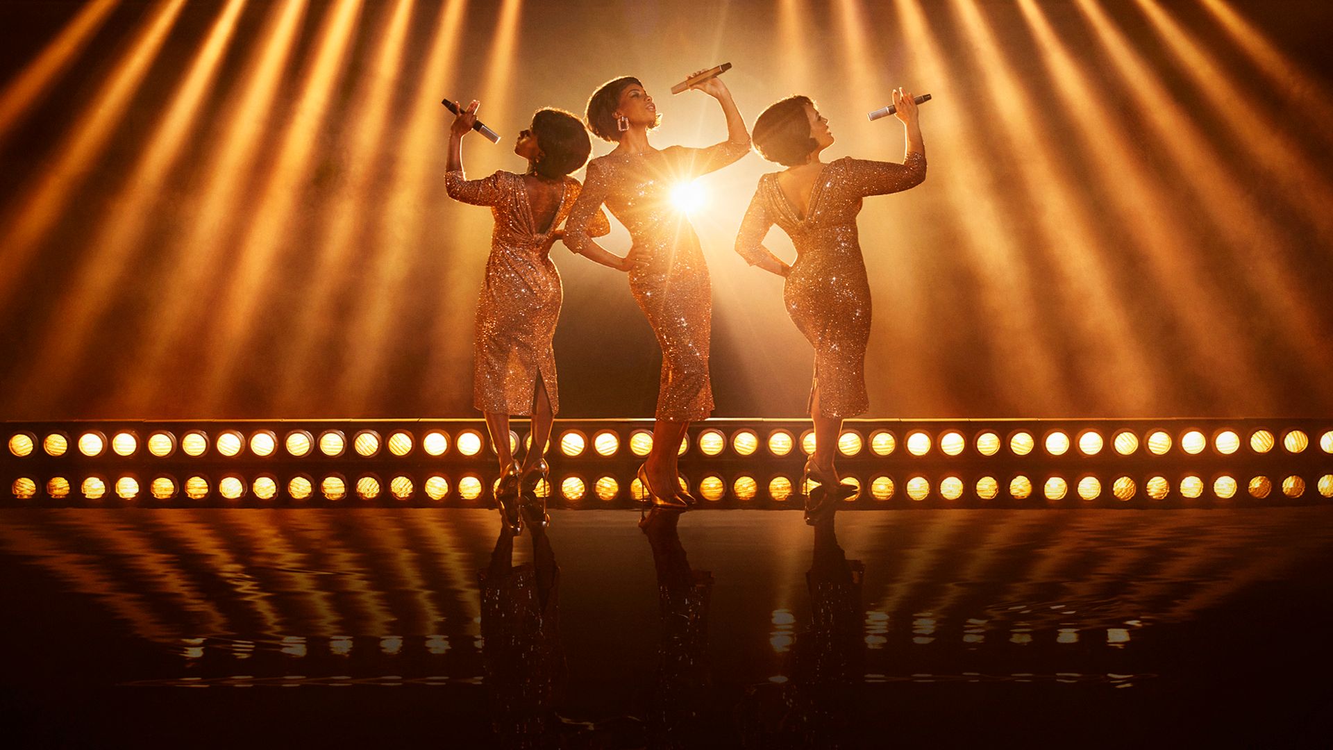 Dreamgirls The Musical manér. Tre tjejer som står i glittriga klänningar.