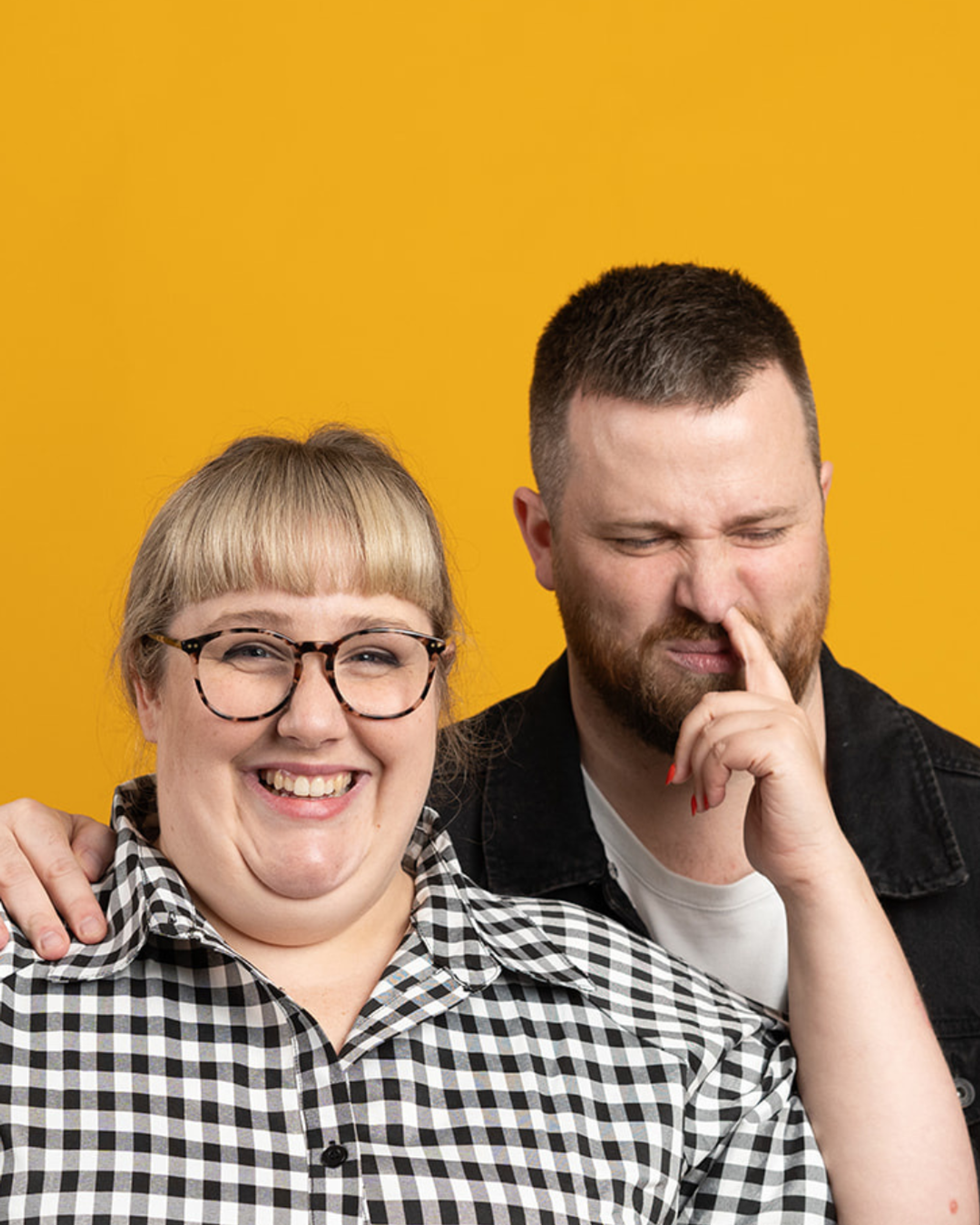 Manér för live podcasten Toni och Ryan. Toni står snett framför Ryan i en svart/vit rutig skjorta och petar Ryan som har en svart skjorta i näsan.