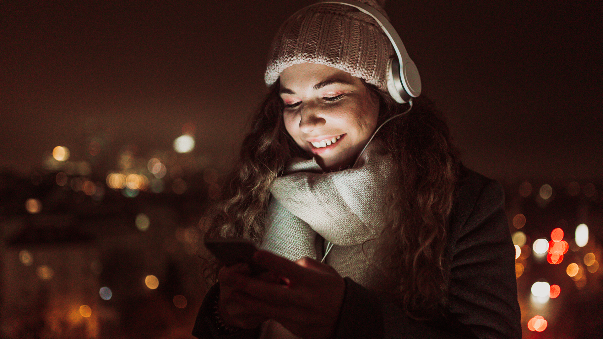 Leende kvinna med hörlurar lyssnar på ljudbok i mobilen – 60 dagar gratis Nextory via Showti