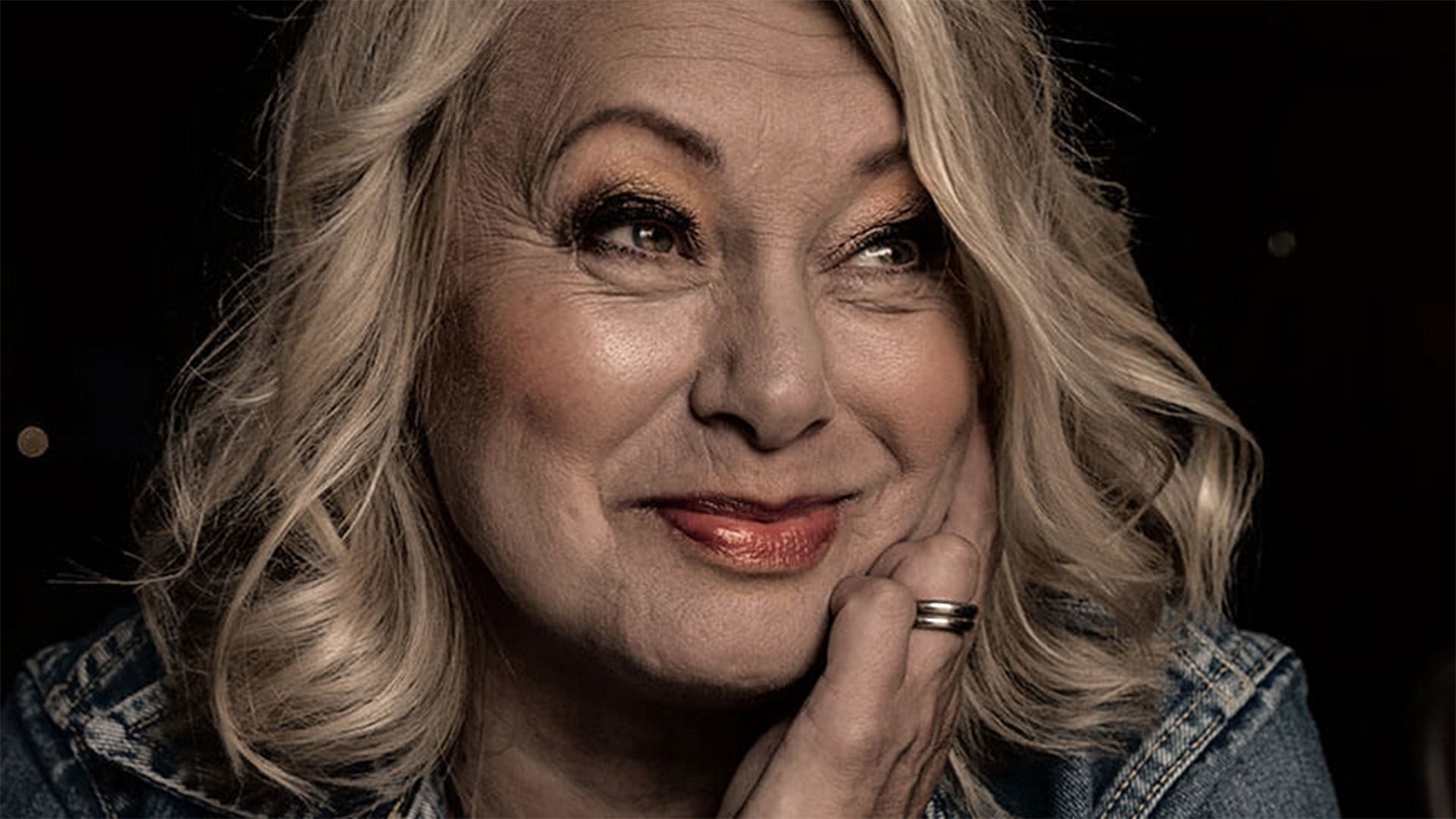 Porträtt på Louise Hoffsten som ler och tittar snett uppåt med en hand på kinden.