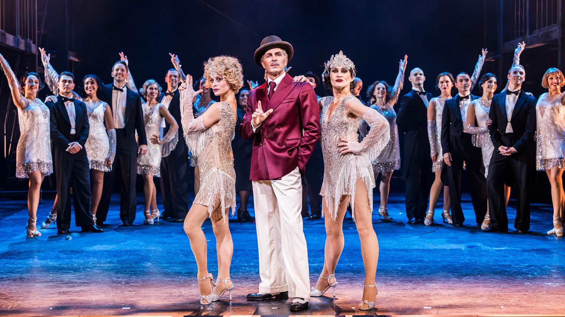 Ellen Lindblad, Peter Jöback och Hanna Lindblad von Spreti i en scen ur musikalen Chicago på Oscarsteatern i Stockholm. De står i centrum framför ensemblen, klädda i eleganta, glittrande scenkostymer. Chicago spelas på Oscarsteatern 16 september–19 december.