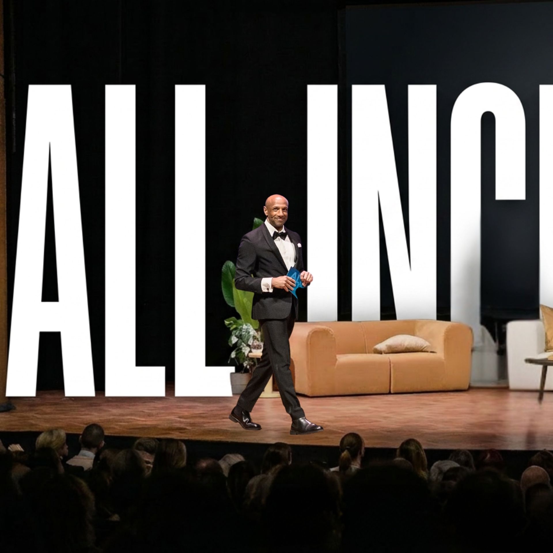 Manér för All Inclusive - Aaron Kroon med gäster. Aaron står på scen med kostym och tittar ut över en publik