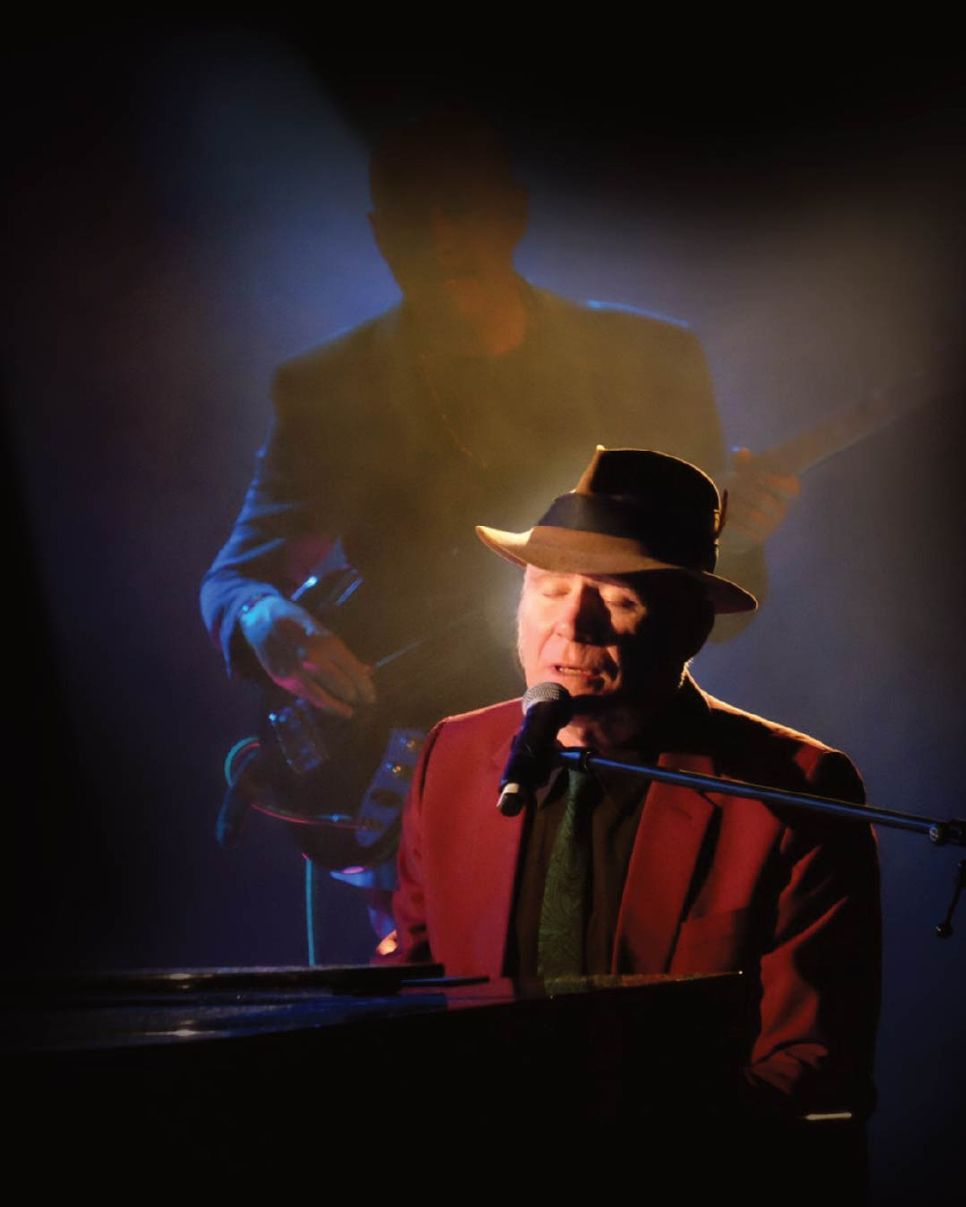 Manér bild för konserten My Leonard Cohen som föreställer Stewart D'Arrietta när han sitter och sjunger vid ett piano under en strålkastare.