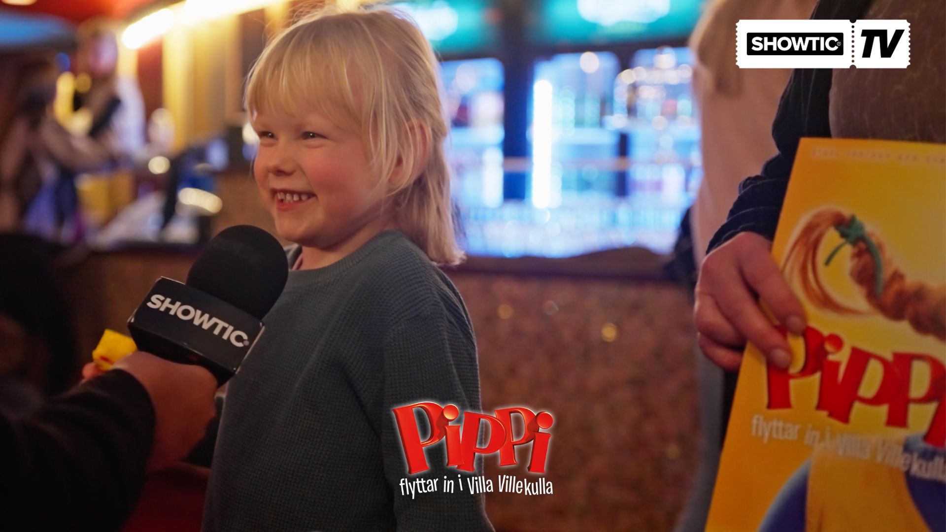 Thumbnail bild för Showtic TV på Pippi flyttar in i Villa Villekulla. En ung tjej står med ett stort leende och prata in i mikrofonen.