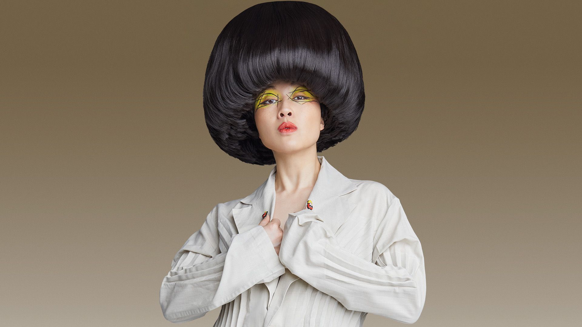 Porträtt av Atsuko Okatsuka i vit kostym, med en stor svart rund frisyr och färgstark ögonmakeup mot en brun bakgrund. The Big Bowl Tour spelas på China Teatern i Stockholm den 16 februari 2027.